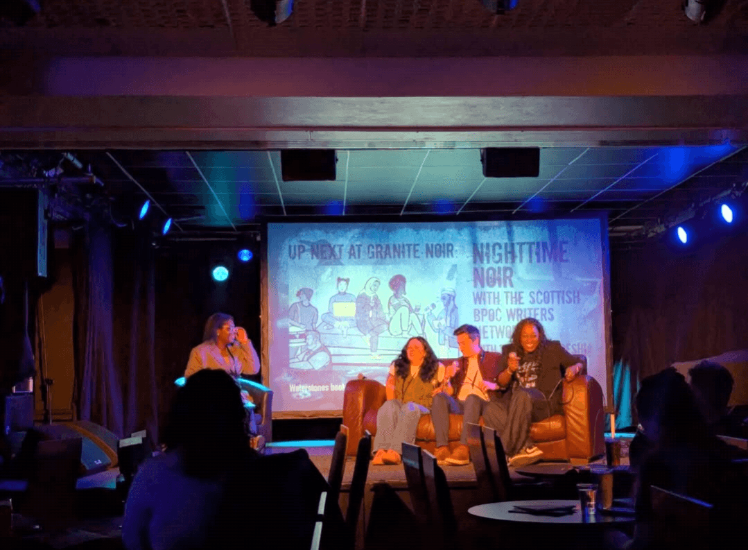 Nailah on stage with three other writers seated on a couch laughing