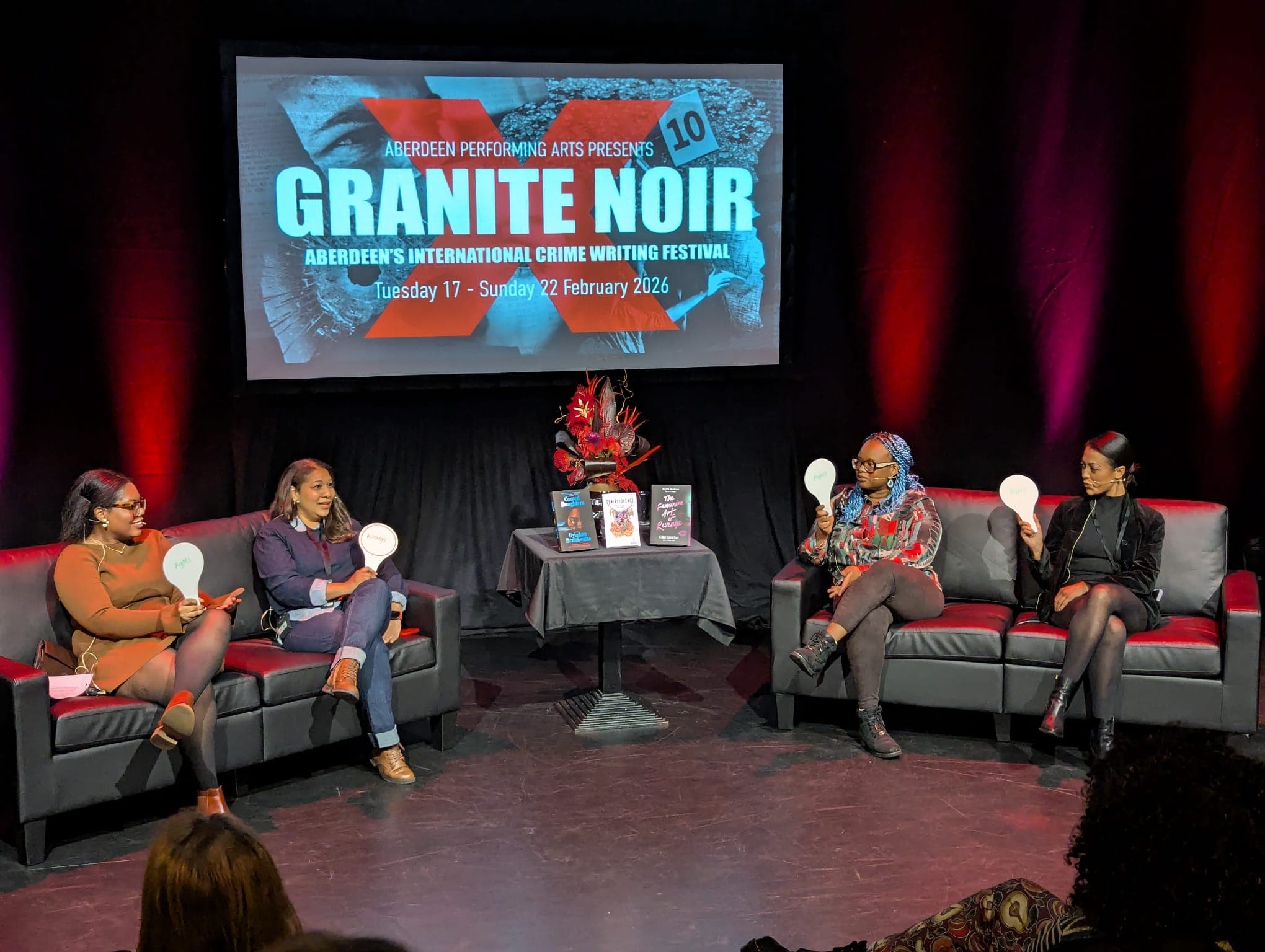 Nailah on stage with three other writers seated on a couch laughing